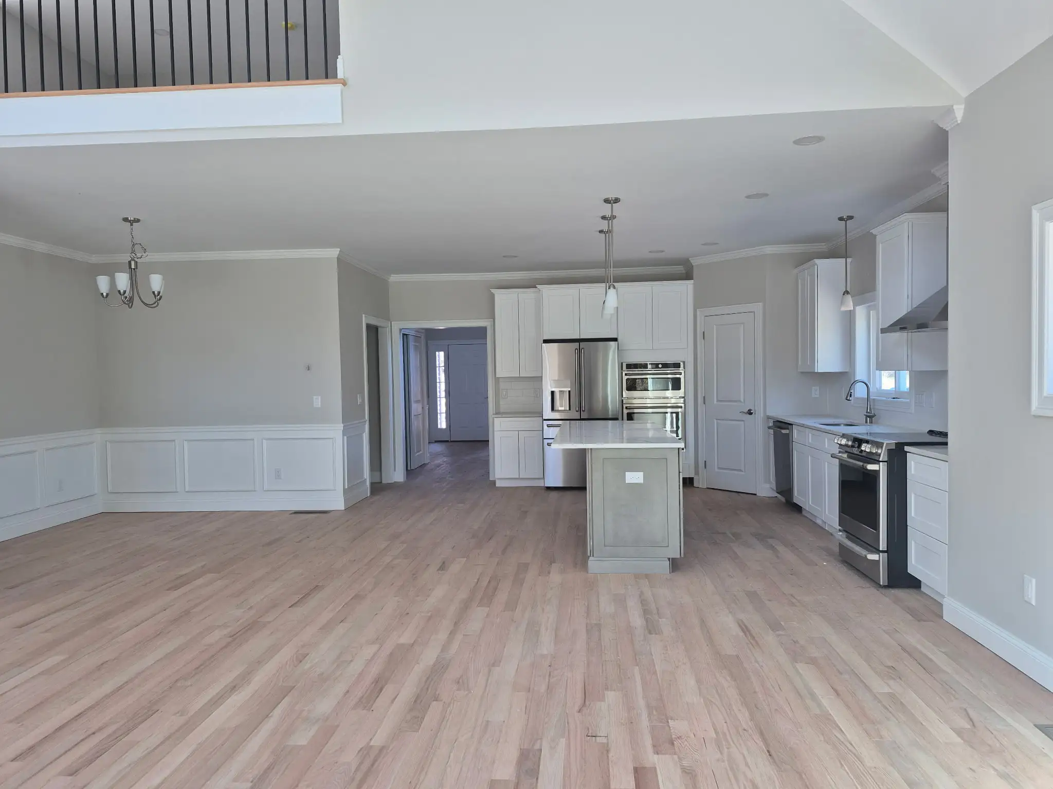 Open-concept kitchen and living space with white cabinets, center island and upper-level balcony