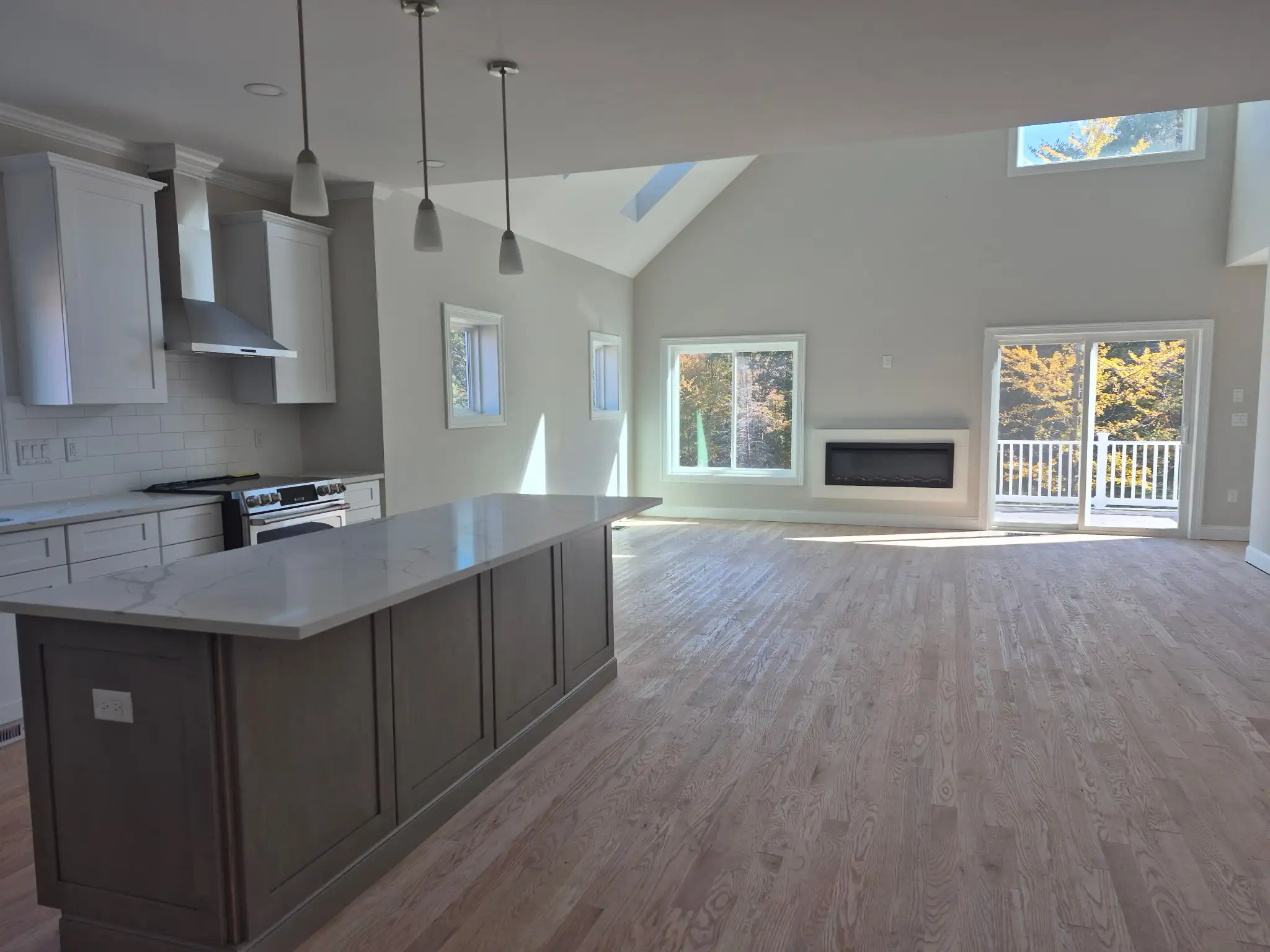 Spacious open-concept living room and kitchen with vaulted ceiling, large windows and fireplace