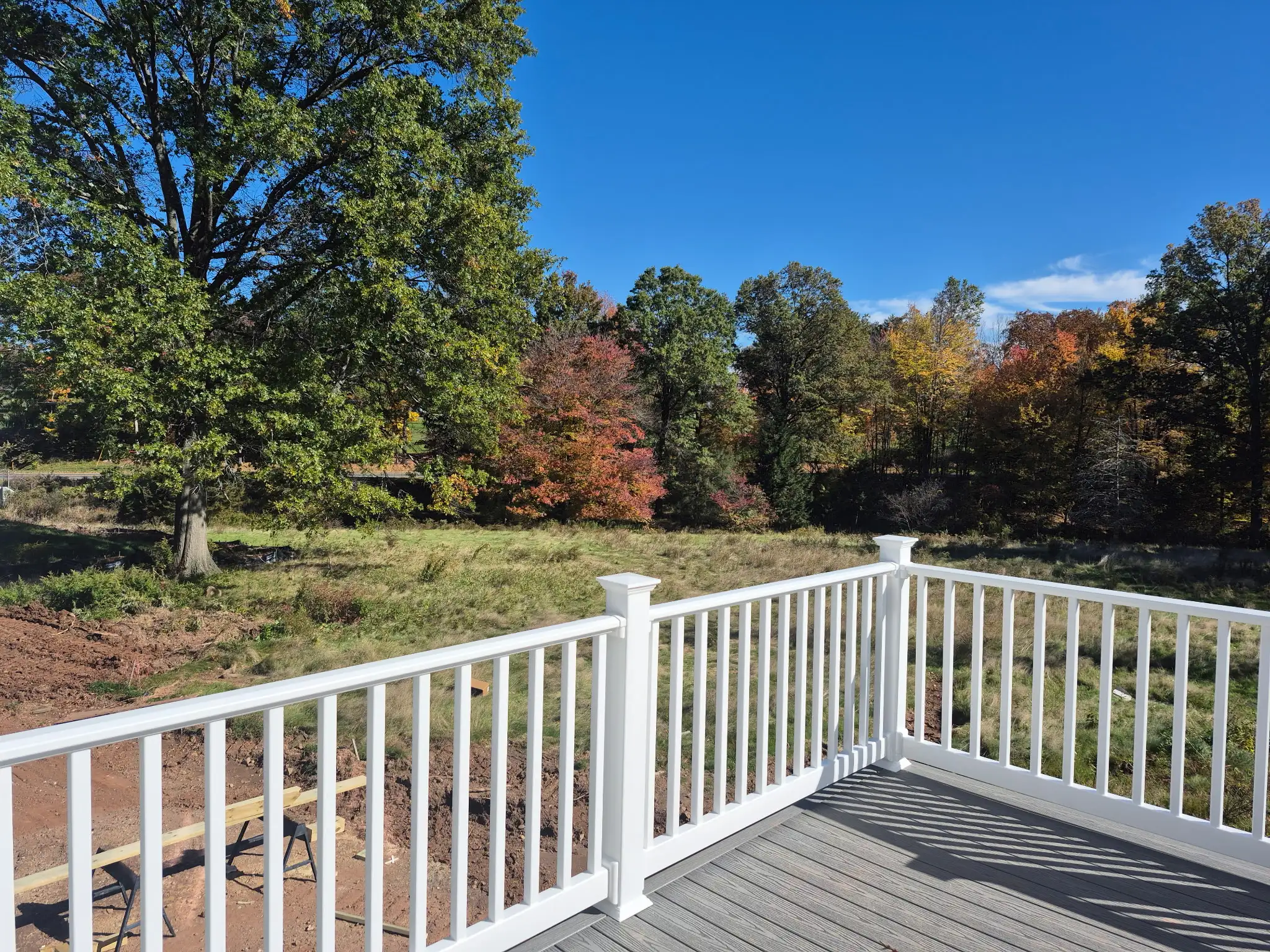 Outdoor deck with white railing overlooking trees and colorful autumn foliage