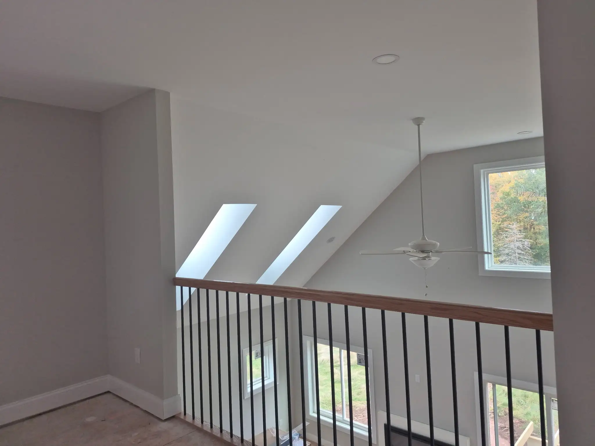 Upper-level landing with white railing, vaulted ceiling, skylights and ceiling fan