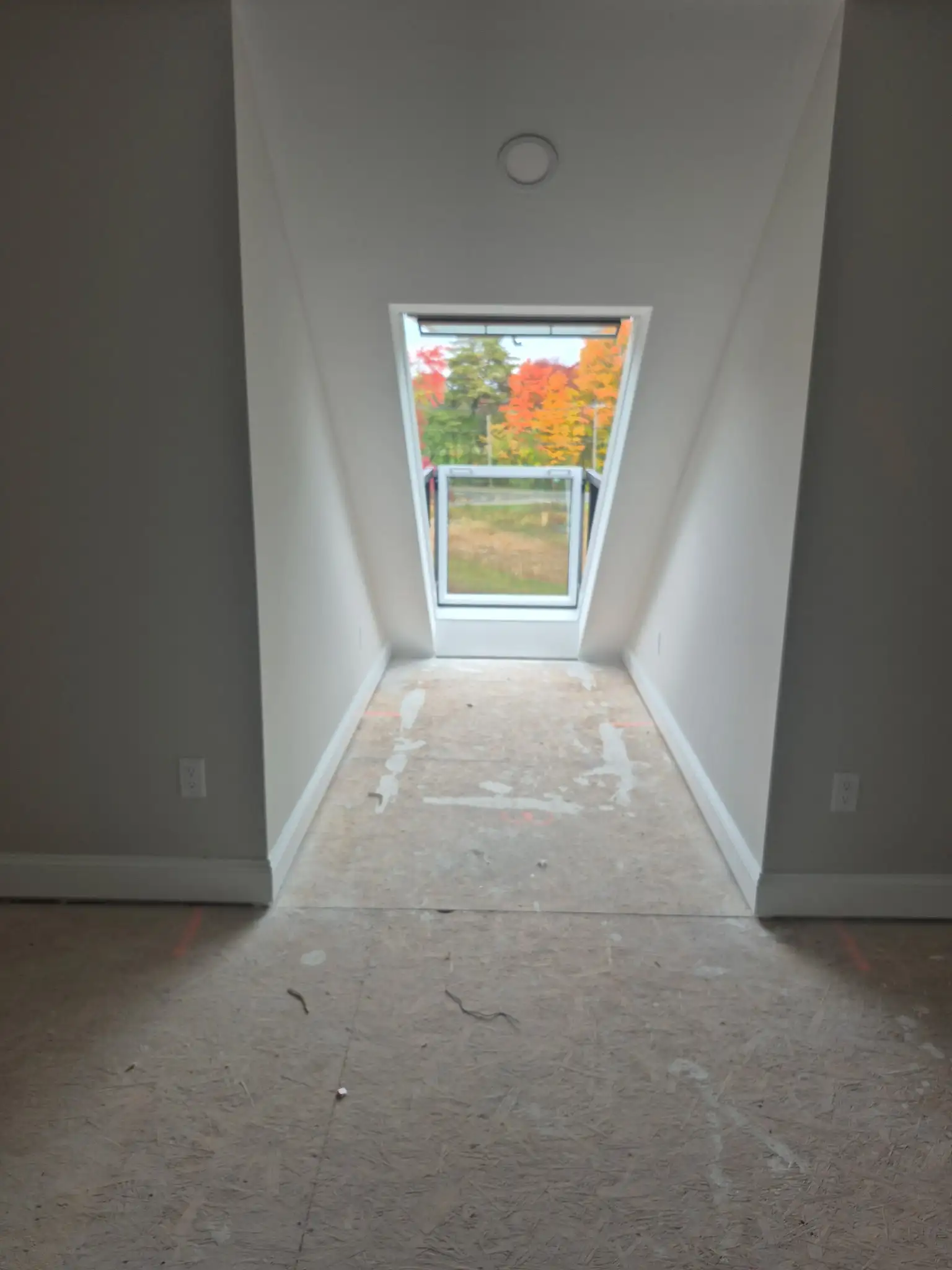 Bright interior hallway with sloped ceiling and window overlooking colorful autumn trees