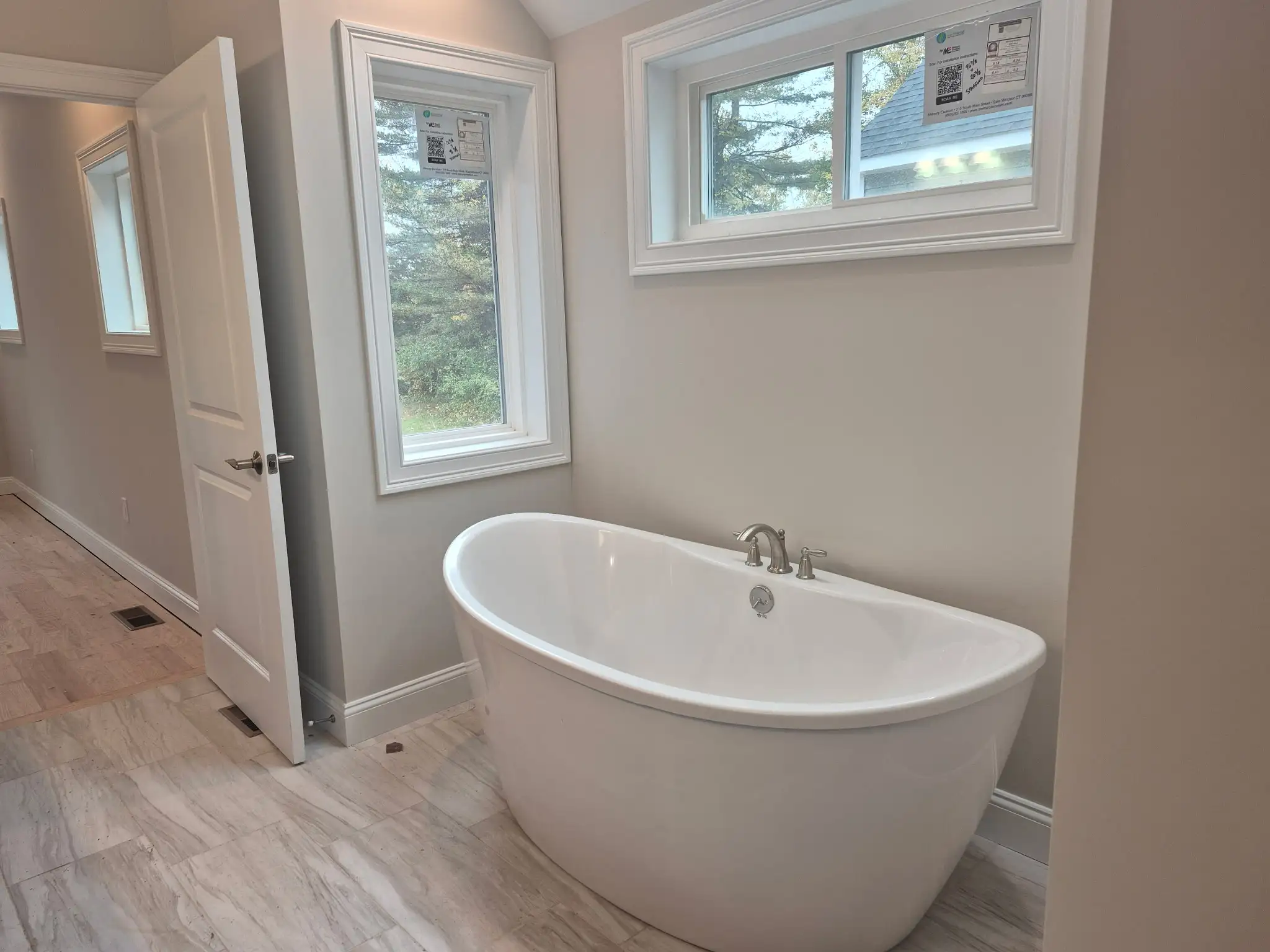 White freestanding soaking bathtub positioned beneath large windows overlooking the outdoors