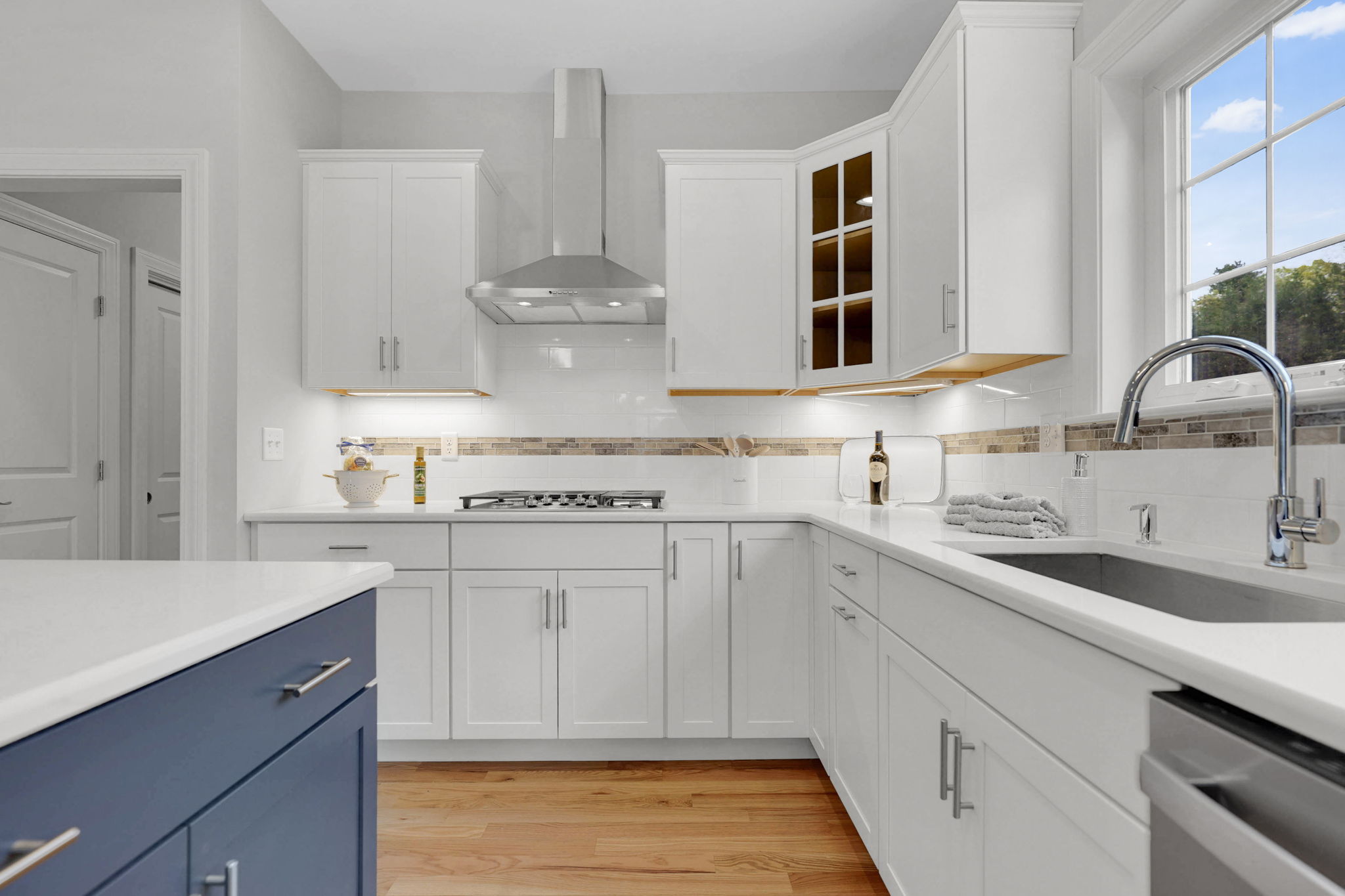 White kitchen with stainless steel range hood, stone countertops and large window
