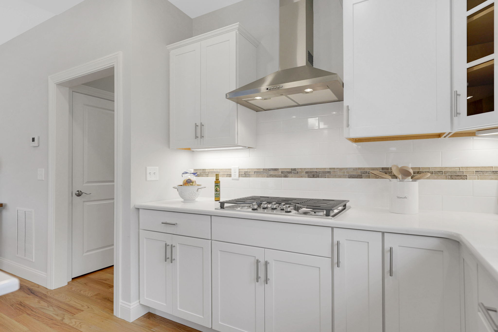 Modern kitchen with white cabinetry, stainless steel range hood and tiled backsplash