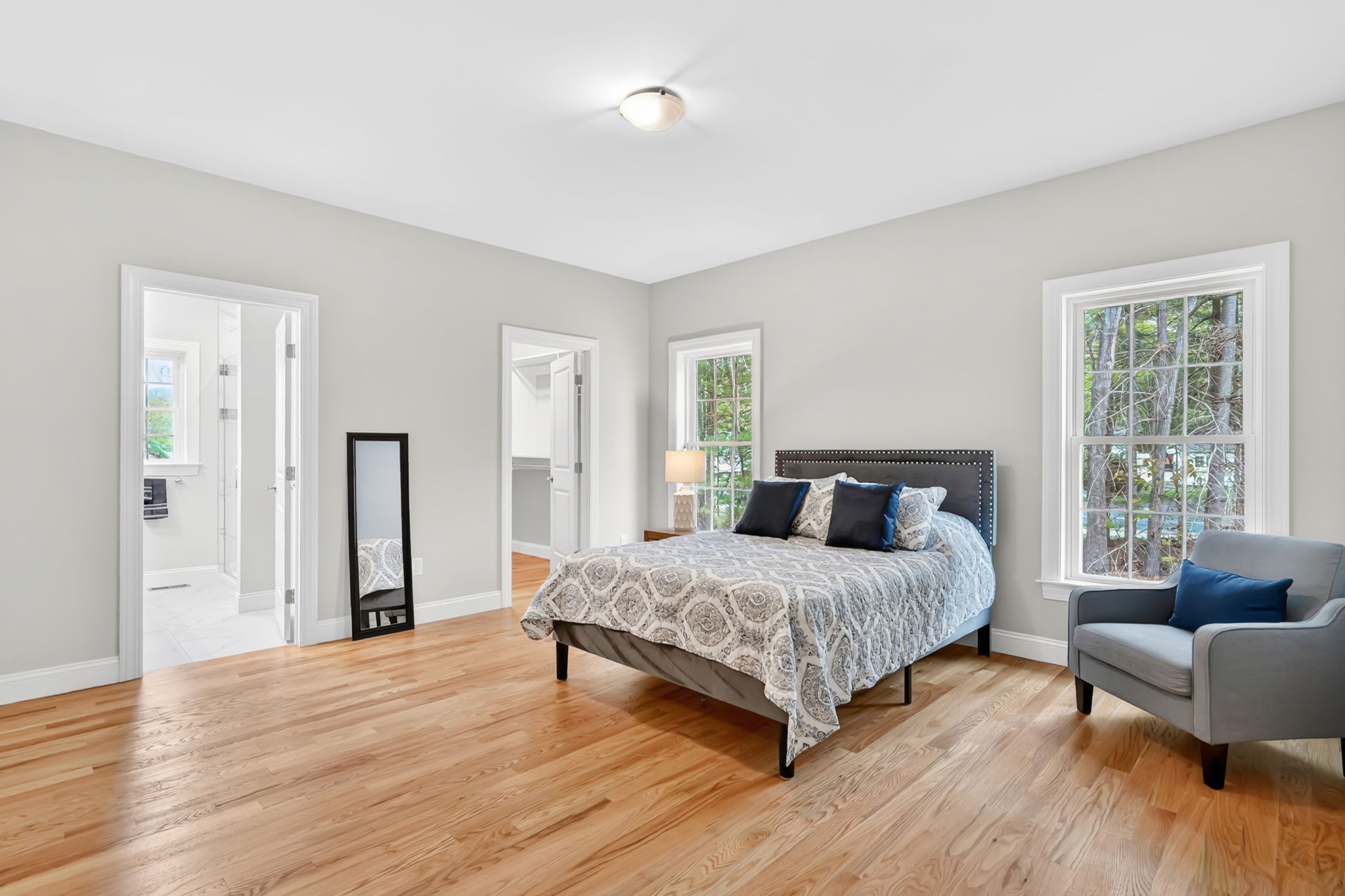 Primary bedroom featuring large windows, hardwood floors, double bed and accent chair