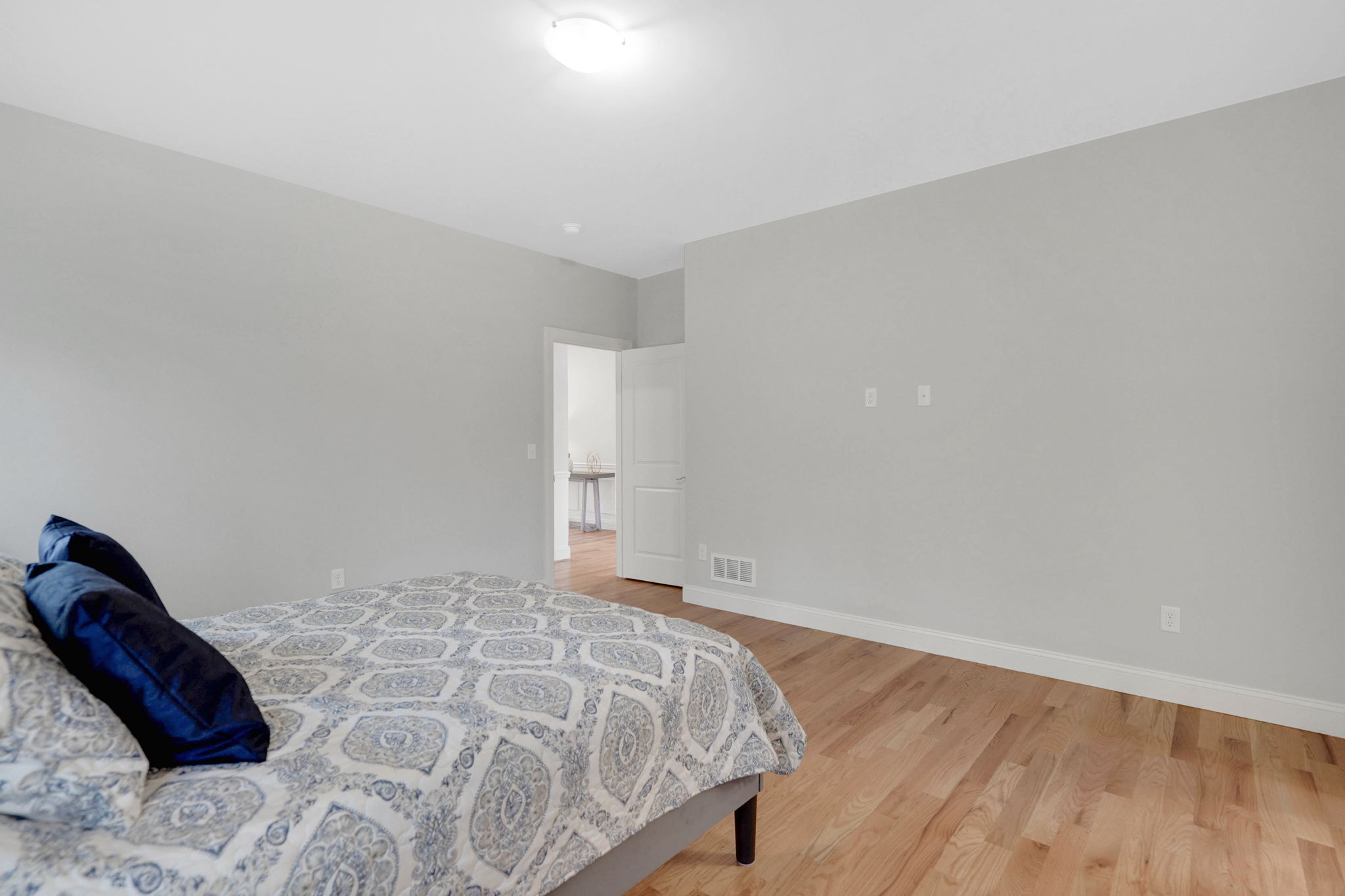 Spacious bedroom with light gray walls, hardwood flooring and doorway to adjoining room