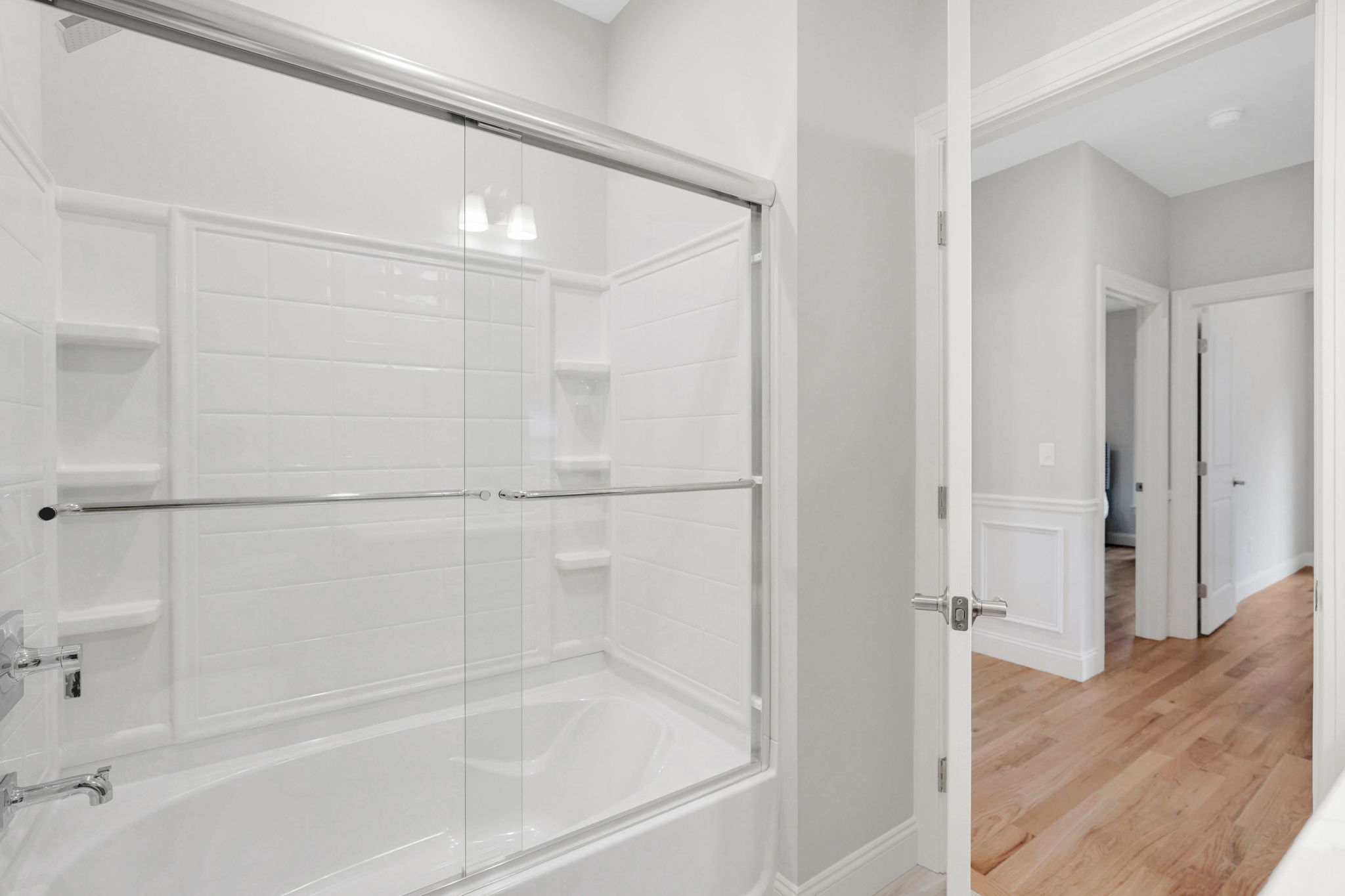Bathroom with white tiled bathtub, glass shower doors and built-in shower shelving