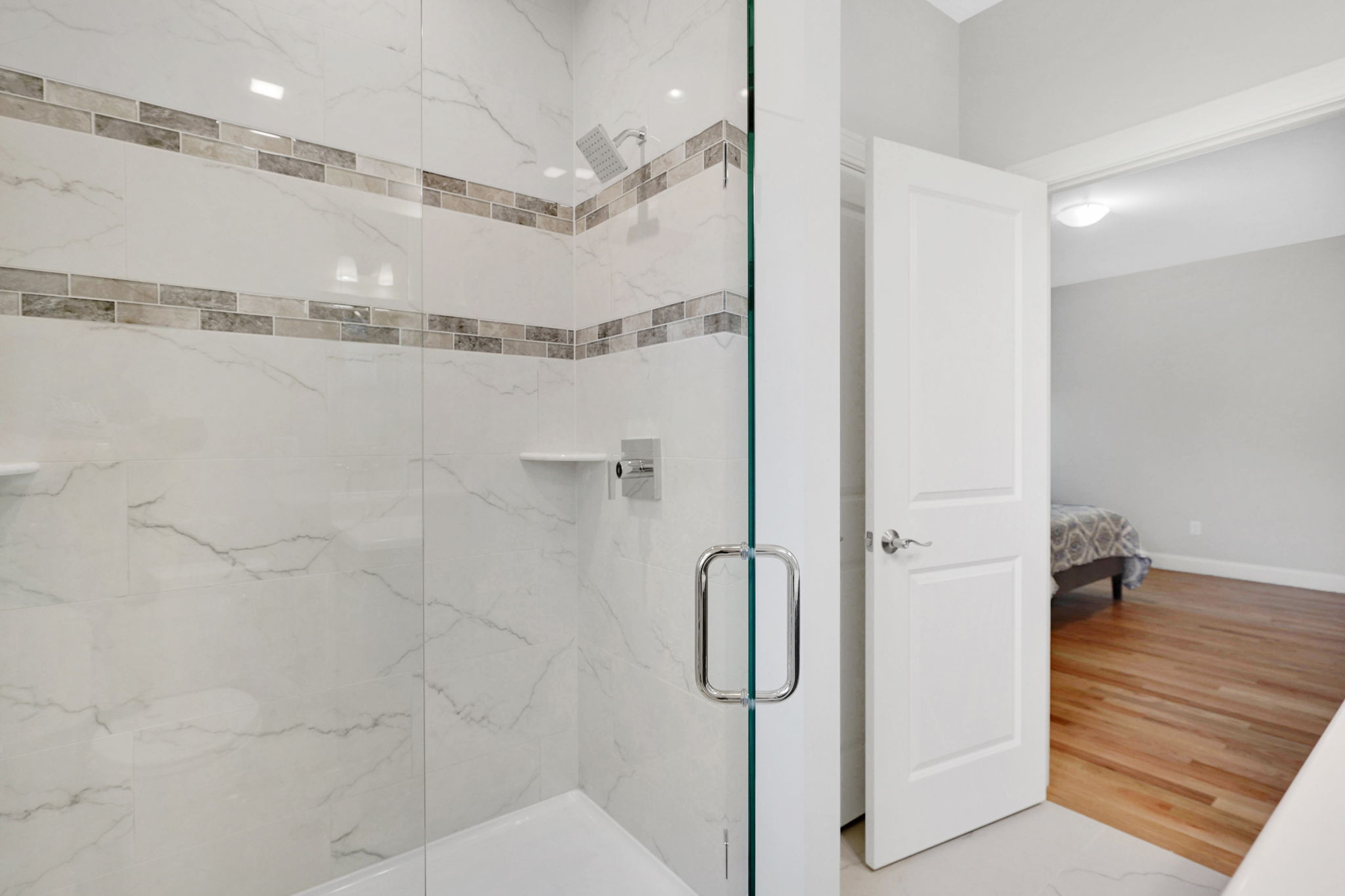 Walk-in shower with glass enclosure, white marble-look tiles and decorative accent bands