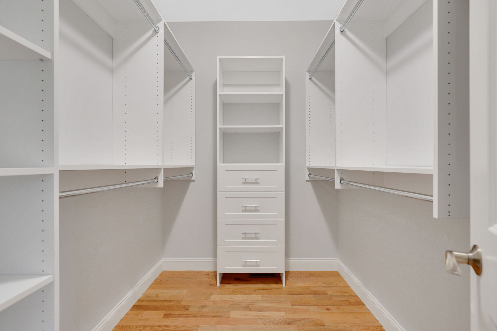 Walk-in closet with white built-in shelving, drawers, hanging space and hardwood floors
