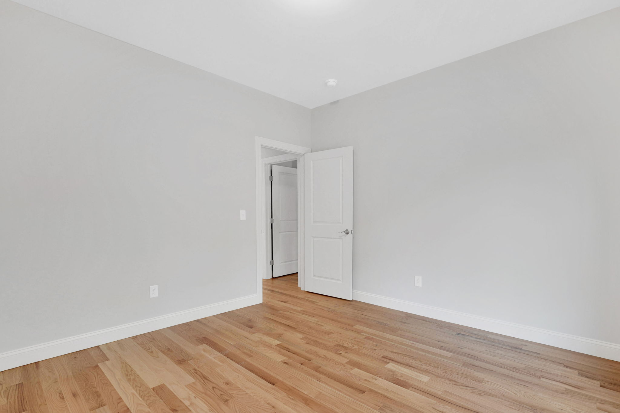 Unfurnished bedroom with light gray walls, recessed ceiling lights and hardwood flooring