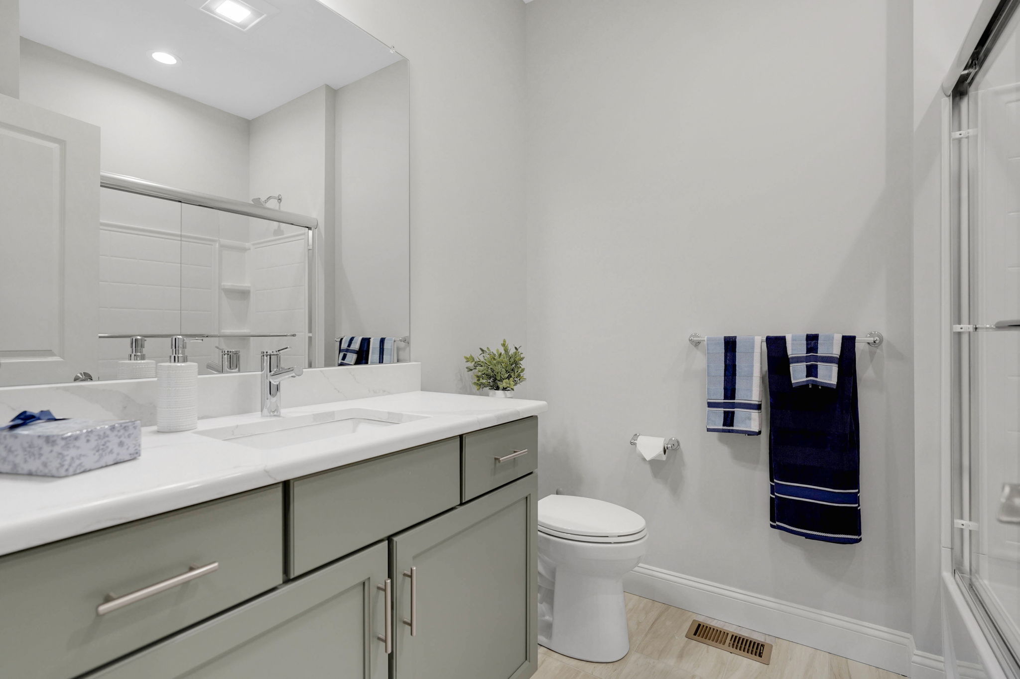 Modern bathroom with gray vanity, white countertop, large mirror and glass-enclosed shower