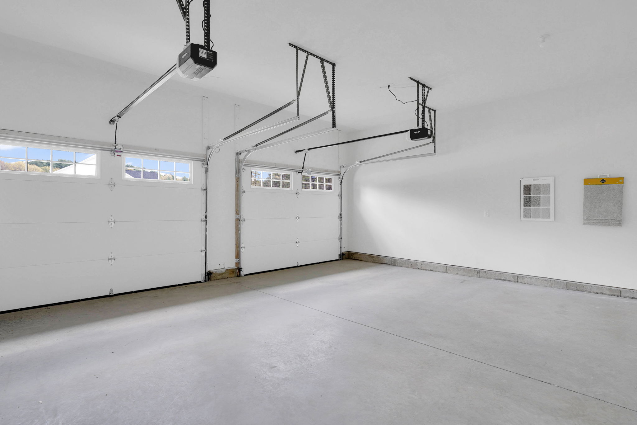 Spacious two-car garage with white overhead doors, automatic openers and concrete flooring