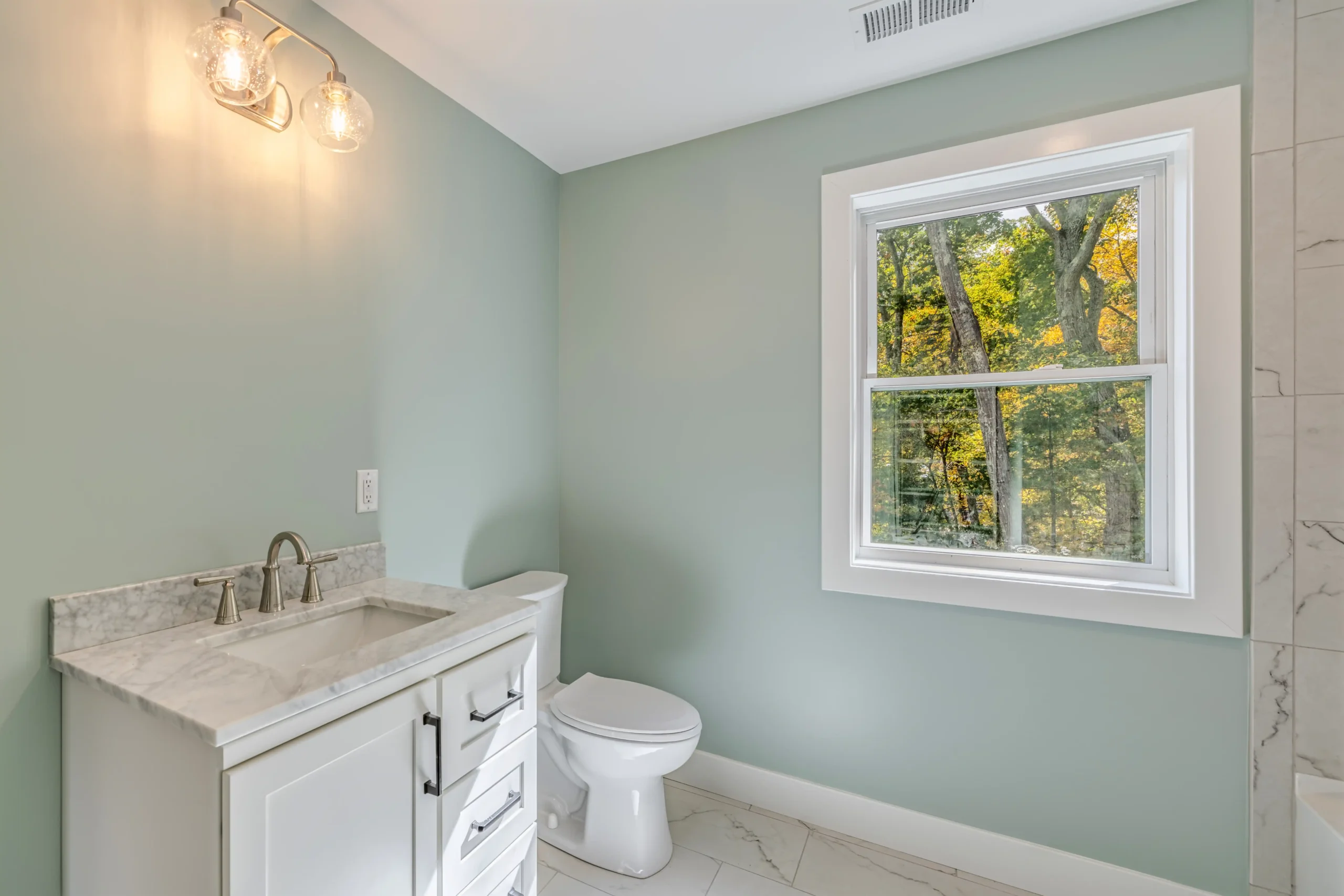 Crystal Lake Home 5 Elm Street Bathroom with pale blue-green walls, white sink and large window overlooking trees