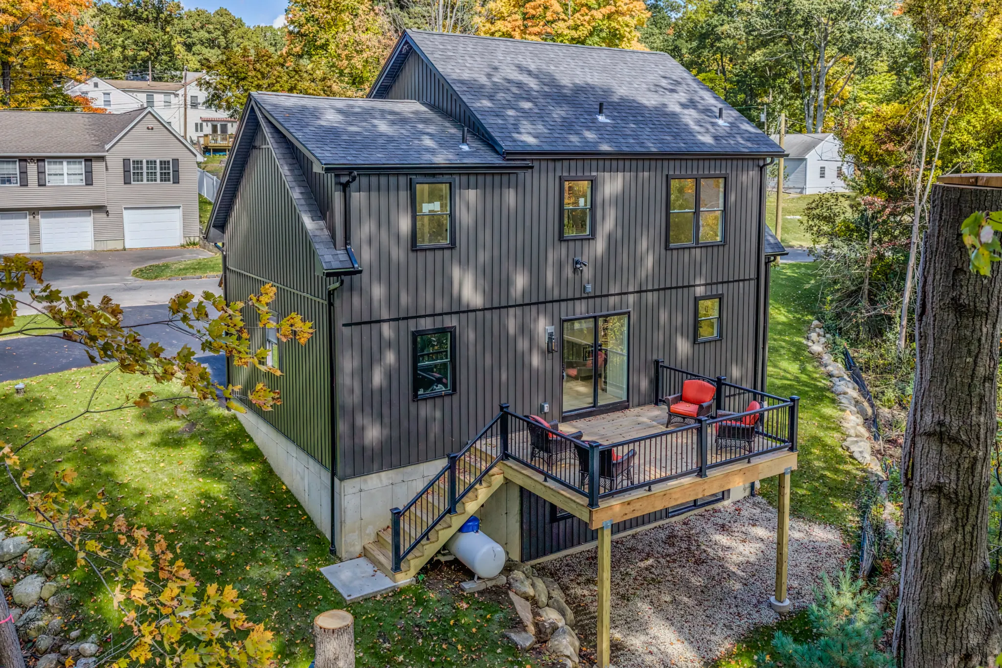 Crystal Lake Home 5 Elm Street Rear exterior of dark gray home with outdoor patio, red chairs and surrounding trees