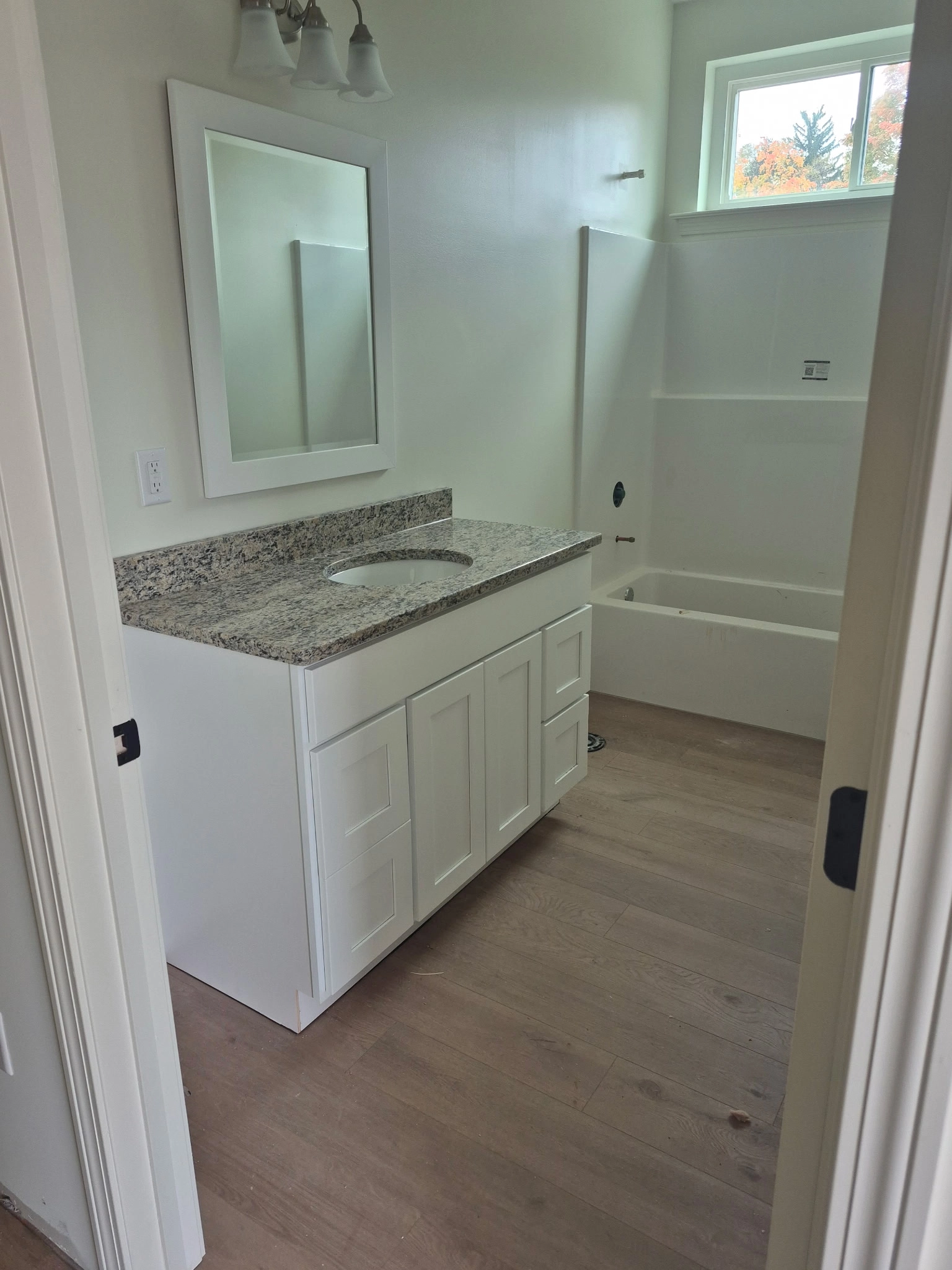 Bathroom with white vanity, granite countertop, framed mirror and bathtub